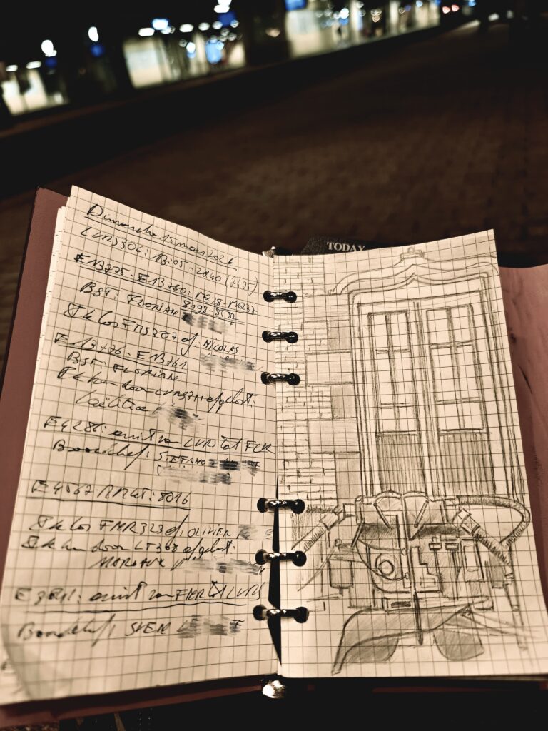 Un carnet ouvert présentant des notes manuscrites et un dessin technique de machines, photographié dans un environnement lumineux.